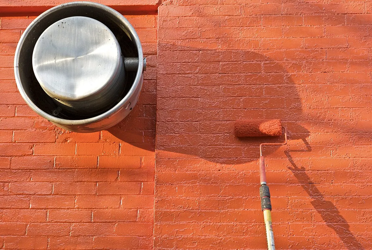 Rodillo pintando una pared de ladrillo de naranja